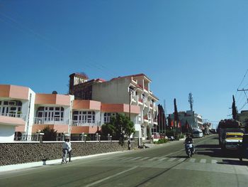 People on street by buildings against clear blue sky