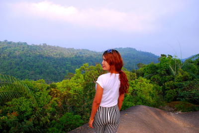 Young woman standing by tree against sky