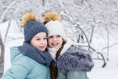 Two smiling girls in warm clothes are hugging in a snowy park. winter walks, lifestyle