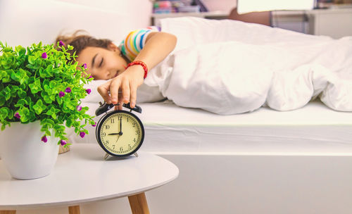 Young woman holding alarm clock on bed at home