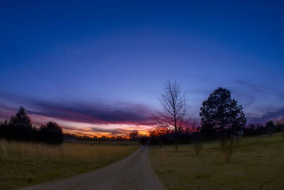 Road amidst bare trees against sky during sunset