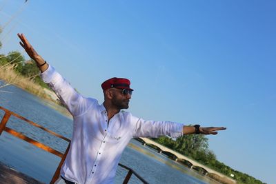 Mid adult man standing with arms outstretched against clear blue sky