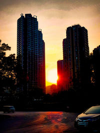 City street by buildings against sky during sunset