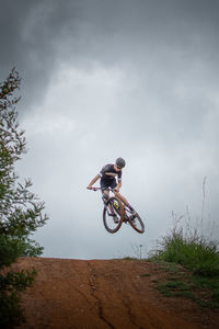 Young adult male riding mountain bike flying through the air, whipping the tail end.  dark clouds