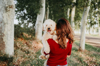 Rear view of woman carrying dog in forest