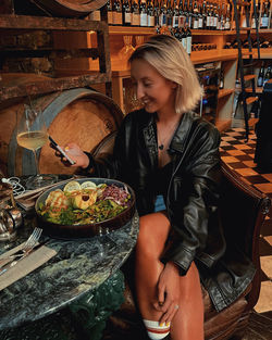 Young woman smiling and looking away while sitting on display in restaurant with wine