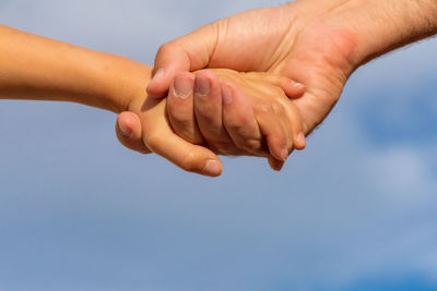 Cropped image of people holding hands against blue sky