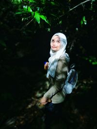 Woman in hijab looking up at forest