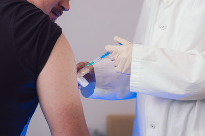 Midsection of doctor injecting syringe in mans hand at clinic