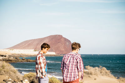 Friends standing at beach against sky