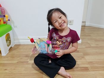 Portrait of cute smiling girl playing with toy while sitting on floor at home
