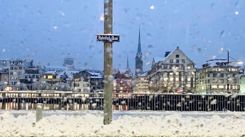 Snow covered buildings in city against sky