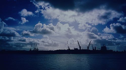 Cranes at harbor against cloudy sky