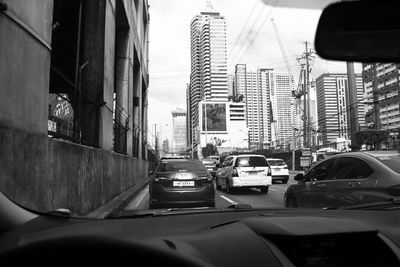 Cars on road amidst buildings seen through car windshield