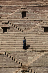 Full length of woman walking on staircase against brick wall