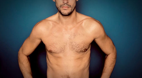 Portrait of shirtless man standing against blue background