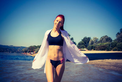 Happy redhead woman in bikini walking through water at the beach during summer day.