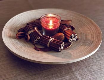 Close-up of illuminated candle with sticks in plate on table