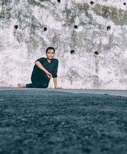 Full length portrait of young man sitting on road