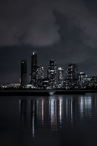 Illuminated buildings by river against sky at night