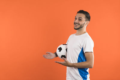 Portrait of young man holding soccer ball against yellow background