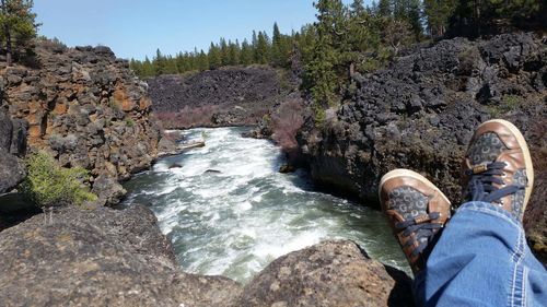 Low section of man sitting on rock at river