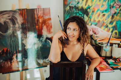 Young female artist sitting at art studio with canvas on background