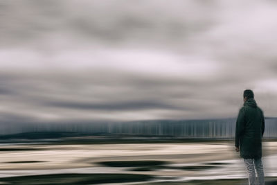 Rear view of man standing on road against cloudy sky