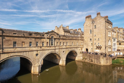 Arch bridge over river by buildings against sky