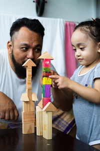 Man looking girl playing with toy blocks