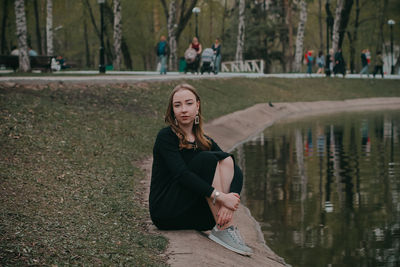 Portrait of woman sitting by lake against trees