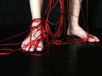 Low section of woman with red strings standing against black background