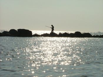 Silhouette man standing in sea against clear sky