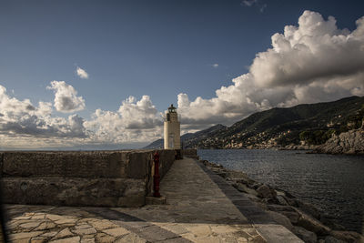 Lighthouse amidst sea and buildings against sky