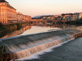 Arch bridge over river amidst buildings against clear sky