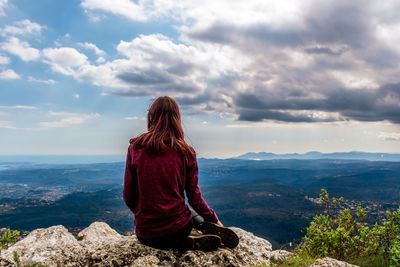 Rear view of woman sitting on rock against sky