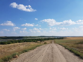 Dirt road amidst field against sky