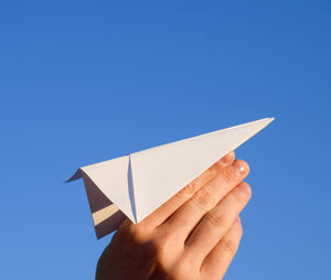 Close-up of hand holding paper against clear blue sky