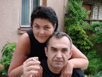 Portrait of woman embracing husband smoking at yard