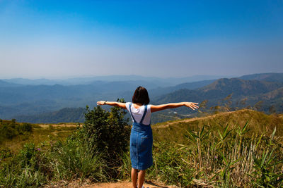 Rear view of woman standing on mountain while looking at landscape against sky