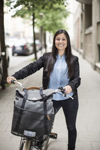 Portrait of happy mid adult businesswoman with bicycle standing on sidewalk