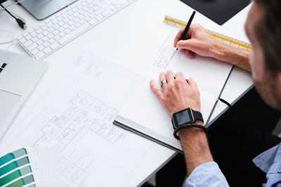 Cropped image of architect writing on diary while planning at desk in creative office