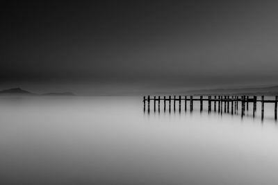 Wooden posts in sea against sky