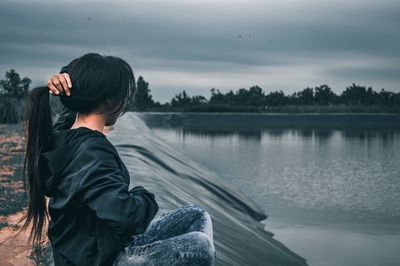 Side view of man sitting by lake against sky