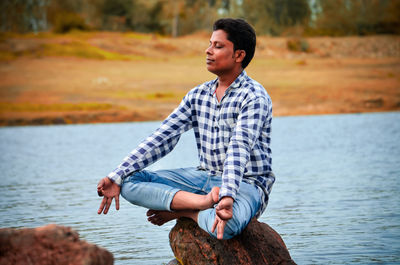 Young man looking away while standing in lake