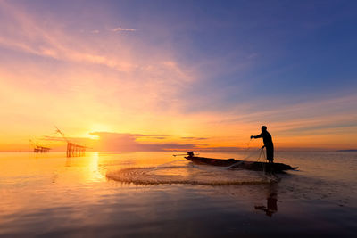 Silhouette of man fishing against sky during sunset