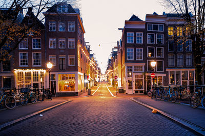 Street amidst illuminated buildings against sky at dusk