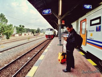 Man and woman standing at railroad station against sky