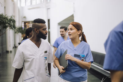 Team of male and female medical experts discussing while walking in hospital lobby