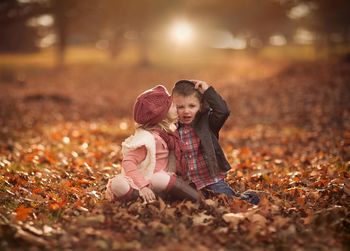 Girl kissing boy sitting on field during autumn